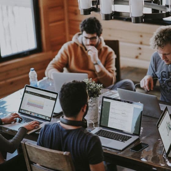 Four people working on laptops at a shared wooden table